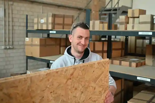 warehouse employee holding wooden board and smiling near storage shelves